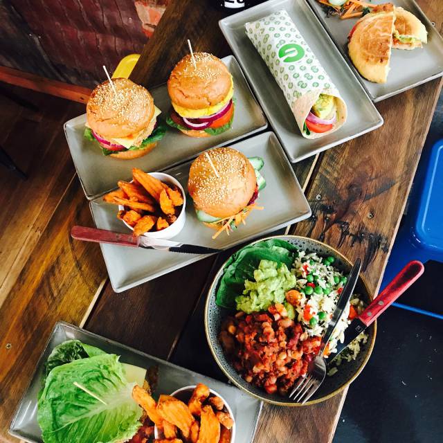 Burger und Wraps mit Salaten auf Holztisch