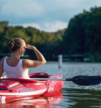 Frau sitzt im Kajak und blickt zum Wald