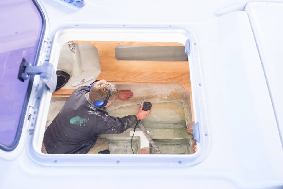 Mann beim Abschleifen von Holz im Innenraum eines Bootes